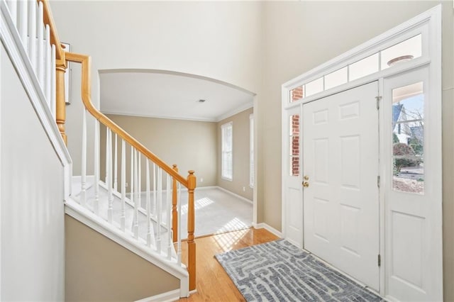 entrance foyer with crown molding, plenty of natural light, a towering ceiling, and light hardwood / wood-style flooring