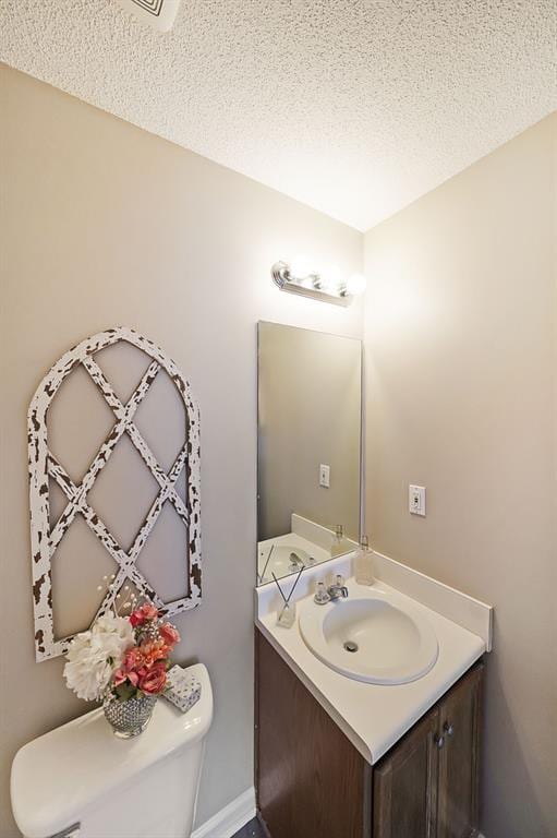 half bath featuring a textured ceiling, vanity, and toilet