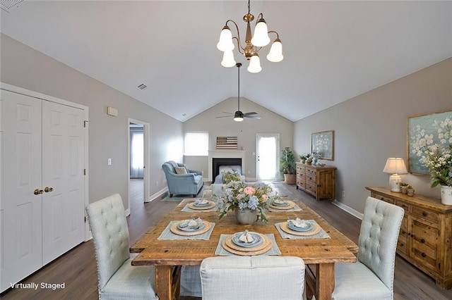 dining space with baseboards, dark wood finished floors, lofted ceiling, a fireplace, and ceiling fan with notable chandelier