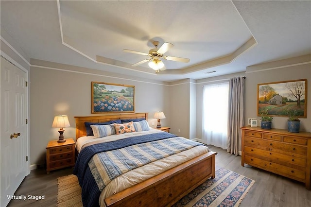 bedroom with visible vents, a raised ceiling, light wood-style floors, and ceiling fan