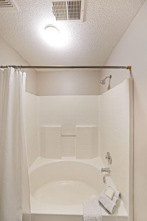 bathroom with visible vents, shower / tub combo with curtain, and a textured ceiling