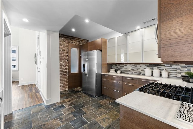 kitchen featuring stainless steel fridge, visible vents, decorative backsplash, glass insert cabinets, and stone finish flooring