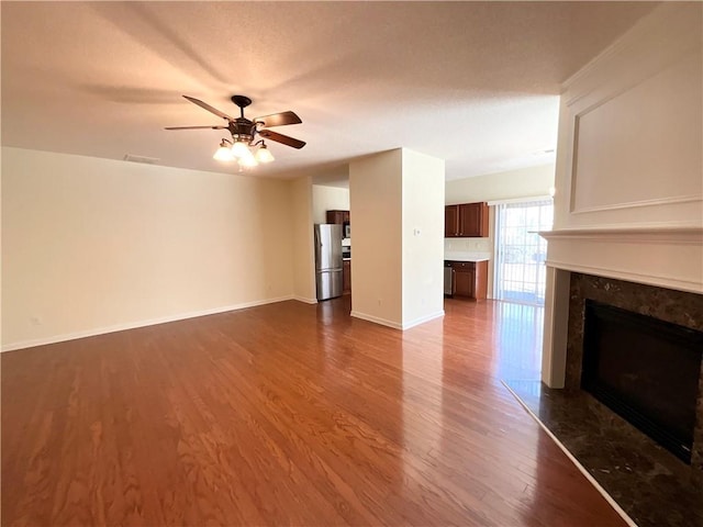 unfurnished living room with a fireplace, visible vents, ceiling fan, wood finished floors, and baseboards