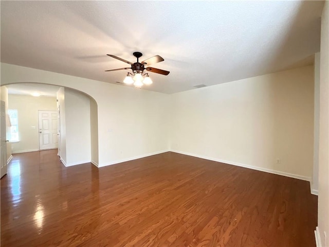 empty room with arched walkways, dark wood finished floors, a ceiling fan, and baseboards