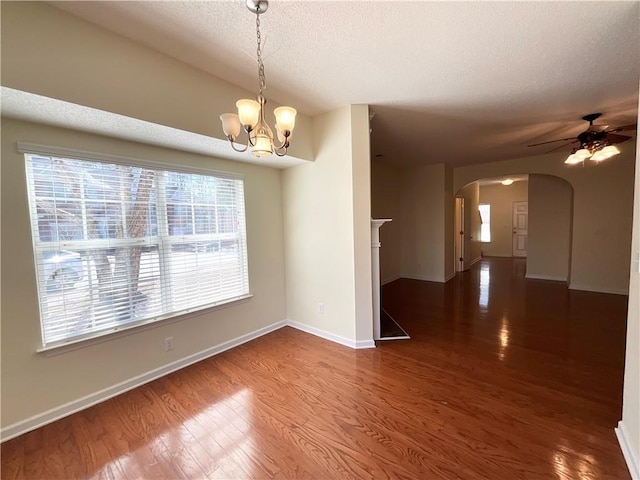 unfurnished room featuring dark wood-style floors, arched walkways, a textured ceiling, baseboards, and ceiling fan with notable chandelier