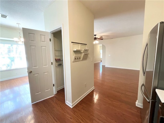 corridor featuring arched walkways, dark wood finished floors, visible vents, an inviting chandelier, and baseboards