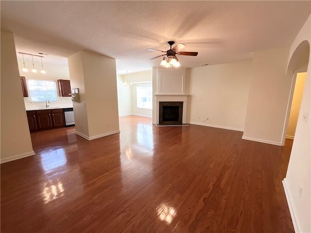 unfurnished living room featuring plenty of natural light, a fireplace with flush hearth, ceiling fan, and dark wood-style flooring