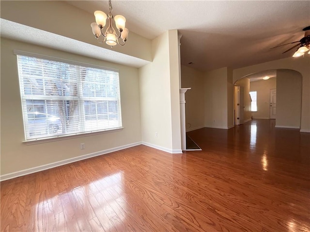 spare room featuring baseboards, arched walkways, wood finished floors, and ceiling fan with notable chandelier