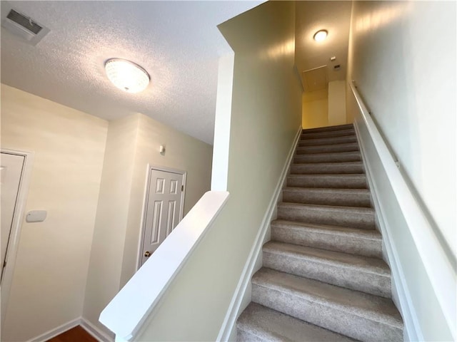 staircase with visible vents and a textured ceiling