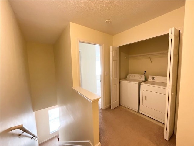 washroom featuring a textured ceiling, washing machine and dryer, light carpet, laundry area, and baseboards