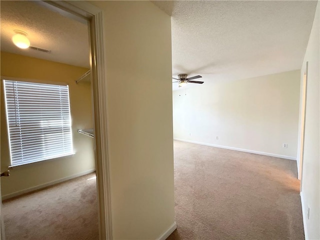 corridor featuring light carpet, baseboards, visible vents, and a textured ceiling