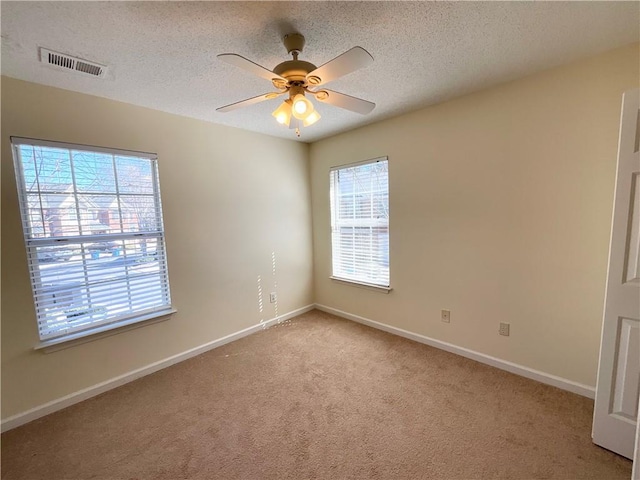 empty room featuring ceiling fan, visible vents, a textured ceiling, and light colored carpet