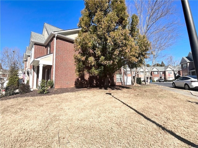 view of property exterior with brick siding, a lawn, and a residential view