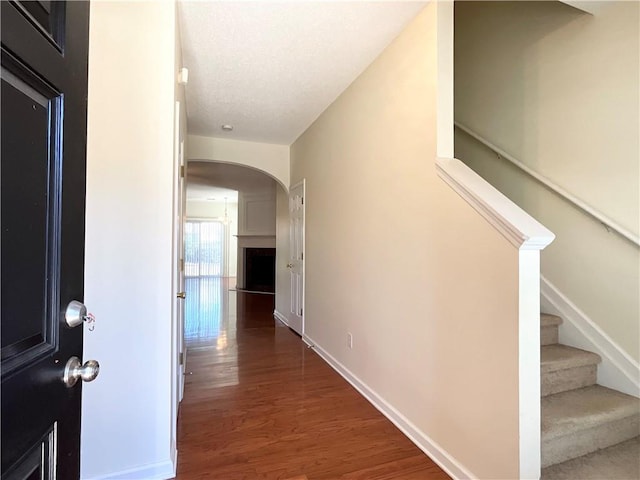 hall featuring baseboards, arched walkways, stairway, wood finished floors, and a textured ceiling