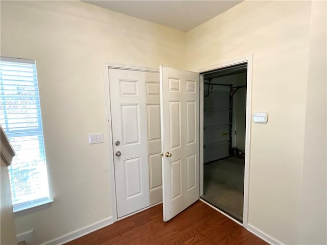 unfurnished bedroom featuring dark wood-style floors, multiple windows, a closet, and baseboards