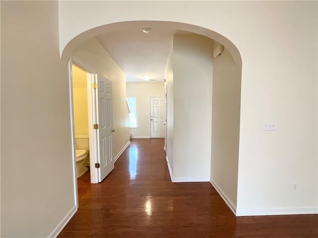 hall featuring arched walkways, dark wood-style flooring, and baseboards