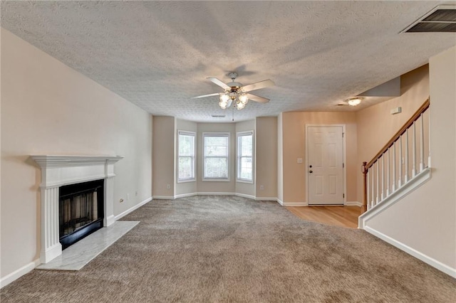 unfurnished living room with carpet, ceiling fan, a textured ceiling, a fireplace with flush hearth, and baseboards