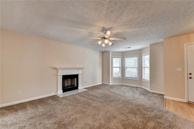 unfurnished living room featuring a textured ceiling, a ceiling fan, carpet, a fireplace, and baseboards