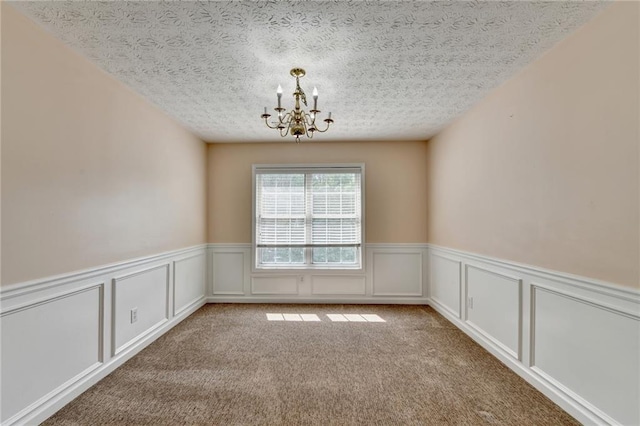 carpeted empty room with a chandelier, a textured ceiling, wainscoting, and a decorative wall