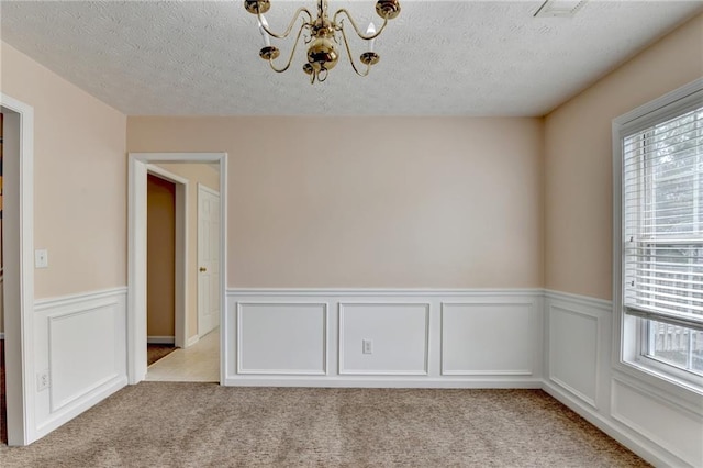 spare room with light carpet, a chandelier, a wainscoted wall, and a textured ceiling