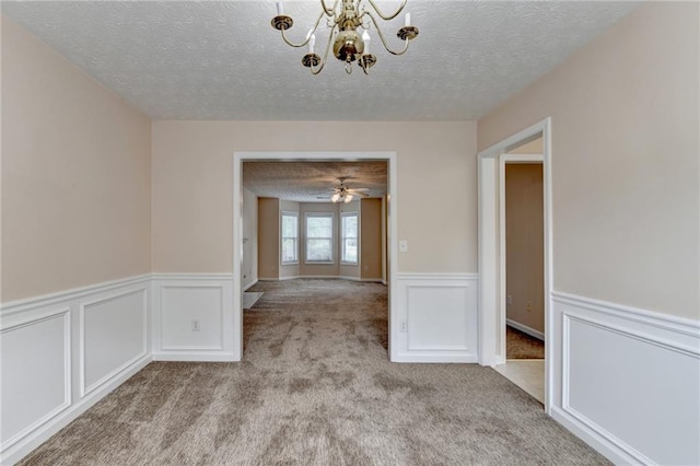 carpeted spare room with a textured ceiling, a chandelier, wainscoting, a decorative wall, and a ceiling fan