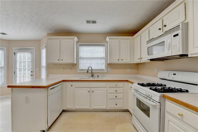 kitchen featuring white appliances, a sink, a peninsula, plenty of natural light, and a textured ceiling