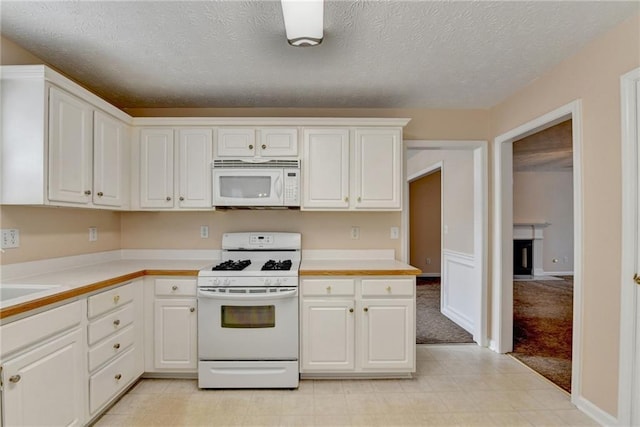 kitchen with white appliances, light countertops, white cabinets, and a textured ceiling
