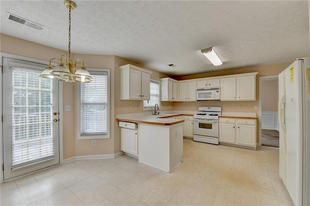 kitchen featuring white appliances, a chandelier, a sink, a peninsula, and light countertops