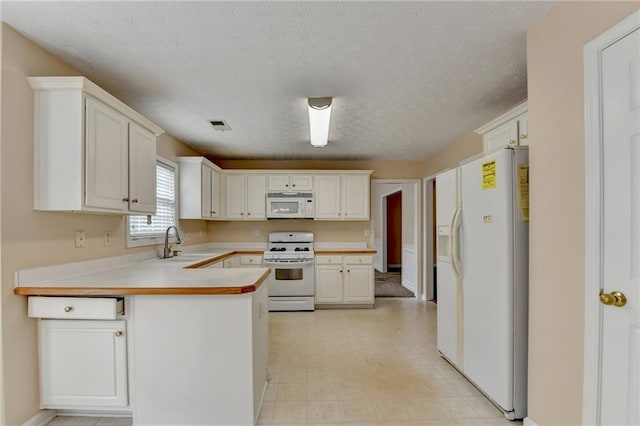 kitchen featuring white appliances, a sink, a peninsula, a textured ceiling, and light countertops