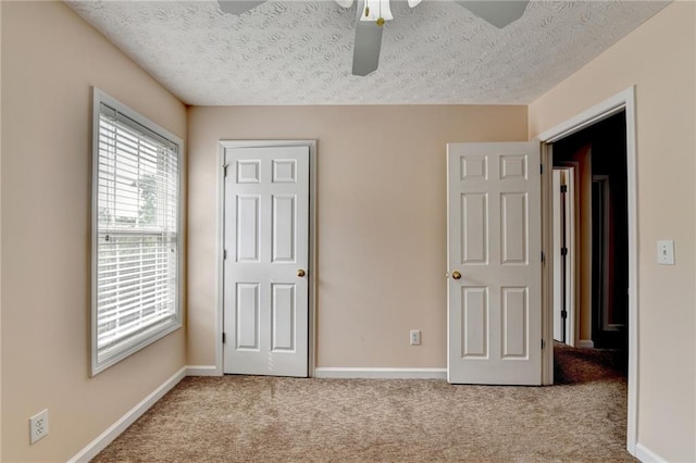 unfurnished bedroom featuring carpet floors, a textured ceiling, baseboards, and a ceiling fan