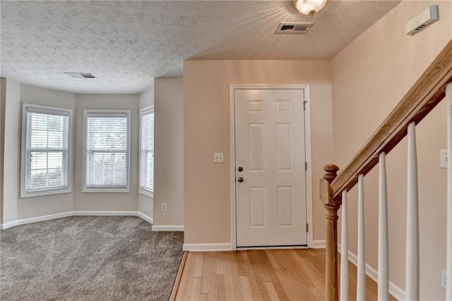 entryway with light wood-type flooring, baseboards, and a textured ceiling