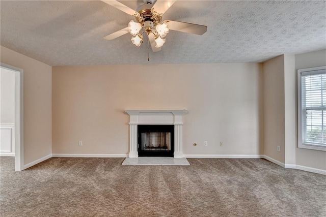 unfurnished living room with a textured ceiling, carpet floors, ceiling fan, a fireplace, and baseboards