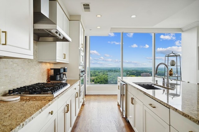 kitchen featuring light stone counters, sink, wall chimney exhaust hood, and appliances with stainless steel finishes