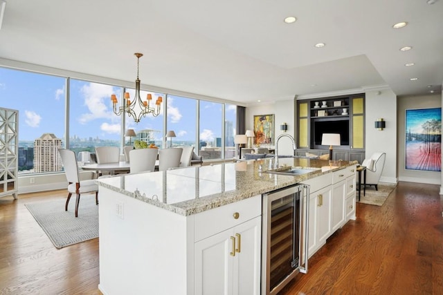 kitchen featuring light stone counters, white cabinetry, wine cooler, and an island with sink