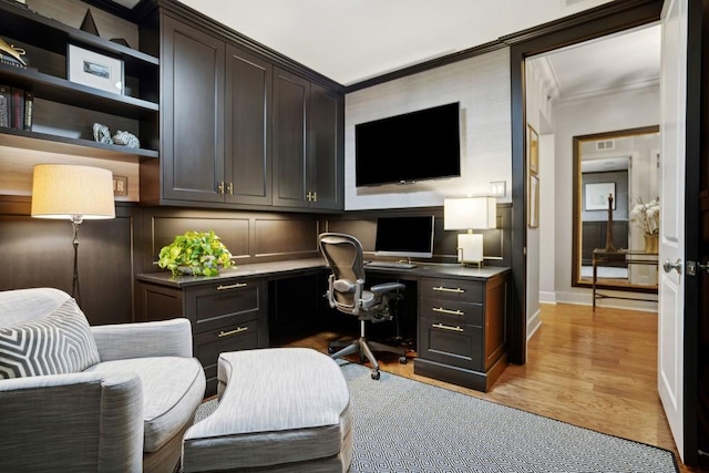 home office featuring built in desk, ornamental molding, and light hardwood / wood-style flooring