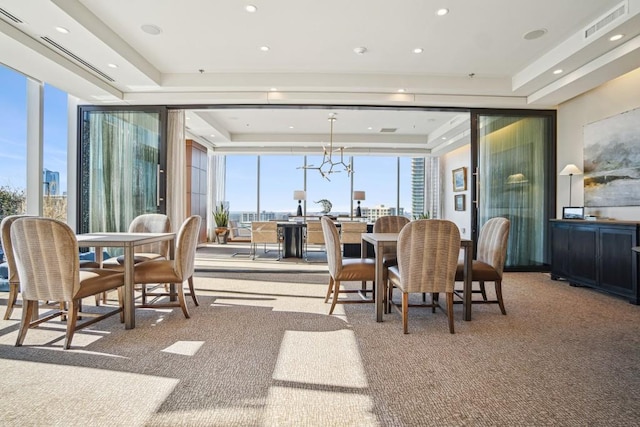 carpeted dining room with an inviting chandelier, a raised ceiling, and a wall of windows