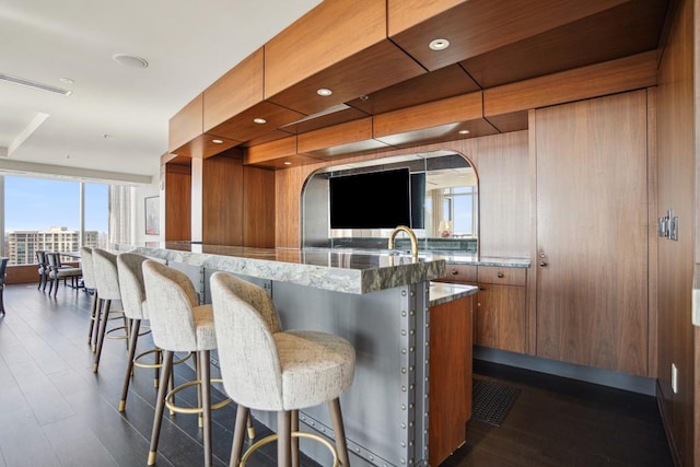 kitchen featuring dark hardwood / wood-style floors, light stone counters, a breakfast bar, and wooden walls