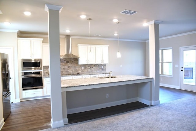 kitchen with white cabinetry, a sink, stainless steel appliances, ornamental molding, and wall chimney exhaust hood