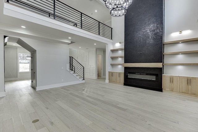 unfurnished living room with stairs, light wood-style floors, a large fireplace, baseboards, and a notable chandelier