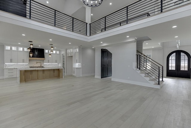 unfurnished living room with stairway, light wood-type flooring, a towering ceiling, baseboards, and recessed lighting