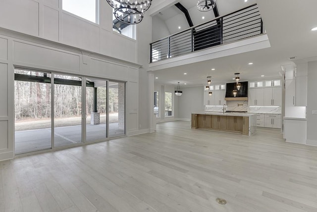 unfurnished living room with a sink, a towering ceiling, light wood finished floors, baseboards, and a notable chandelier