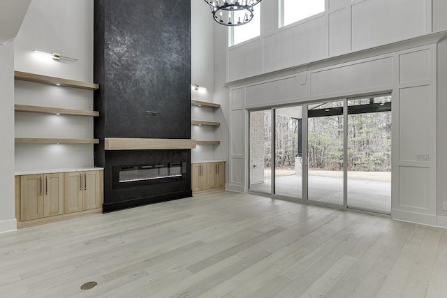 unfurnished living room with a glass covered fireplace, a towering ceiling, an inviting chandelier, and light wood-style floors