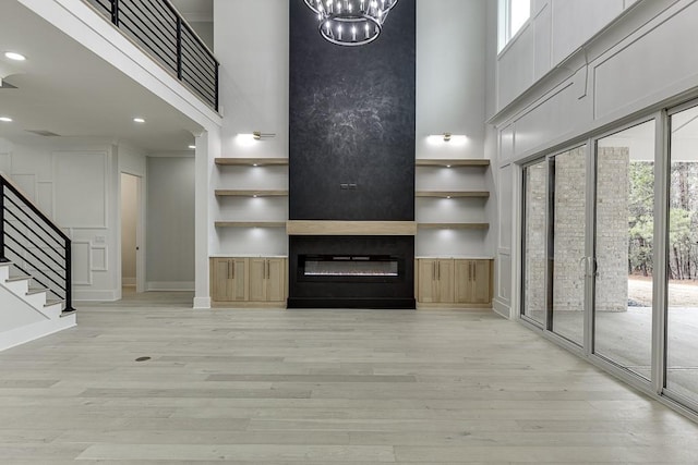 unfurnished living room featuring stairs, light wood-style floors, built in features, a large fireplace, and a high ceiling