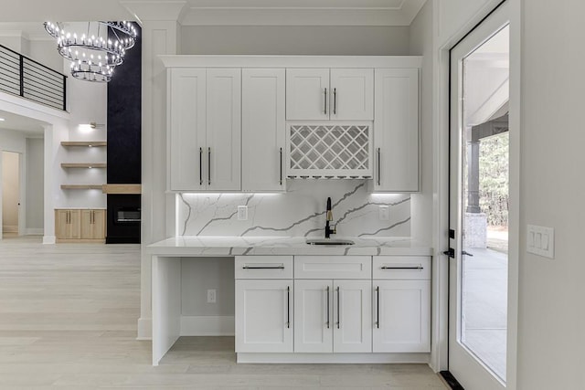 interior space with indoor wet bar, an inviting chandelier, a sink, and light wood-type flooring