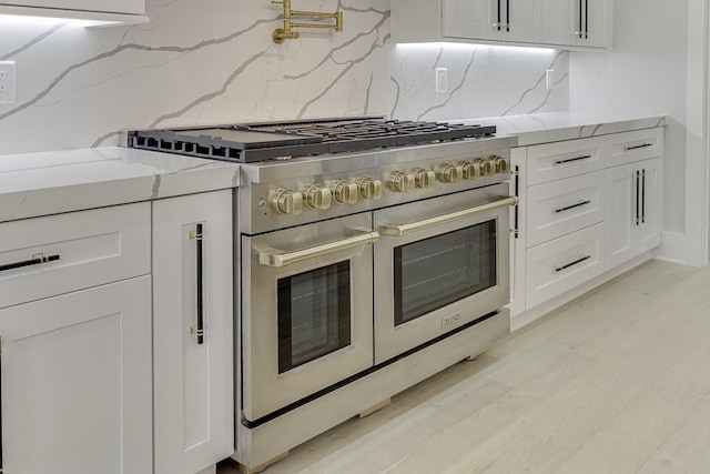 kitchen featuring light wood finished floors, white cabinets, double oven range, decorative backsplash, and light stone counters