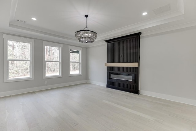 unfurnished living room featuring ornamental molding, a notable chandelier, a tray ceiling, and light wood finished floors