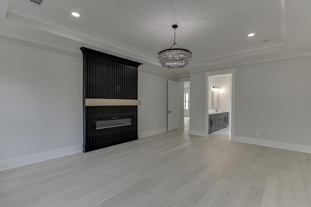 unfurnished living room featuring an inviting chandelier, crown molding, a tray ceiling, and light wood-type flooring