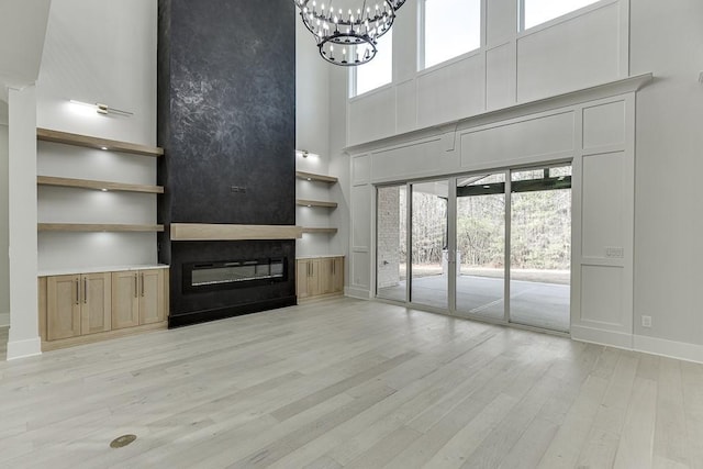 unfurnished living room featuring light wood finished floors, a towering ceiling, a healthy amount of sunlight, a chandelier, and a large fireplace