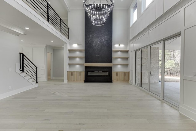 unfurnished living room featuring light wood finished floors, a towering ceiling, a large fireplace, stairway, and crown molding