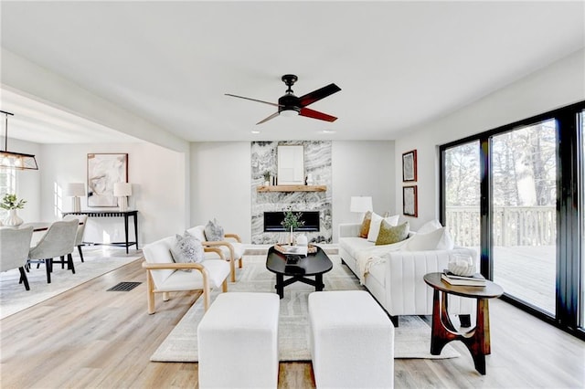 living area with visible vents, light wood finished floors, ceiling fan, and a large fireplace